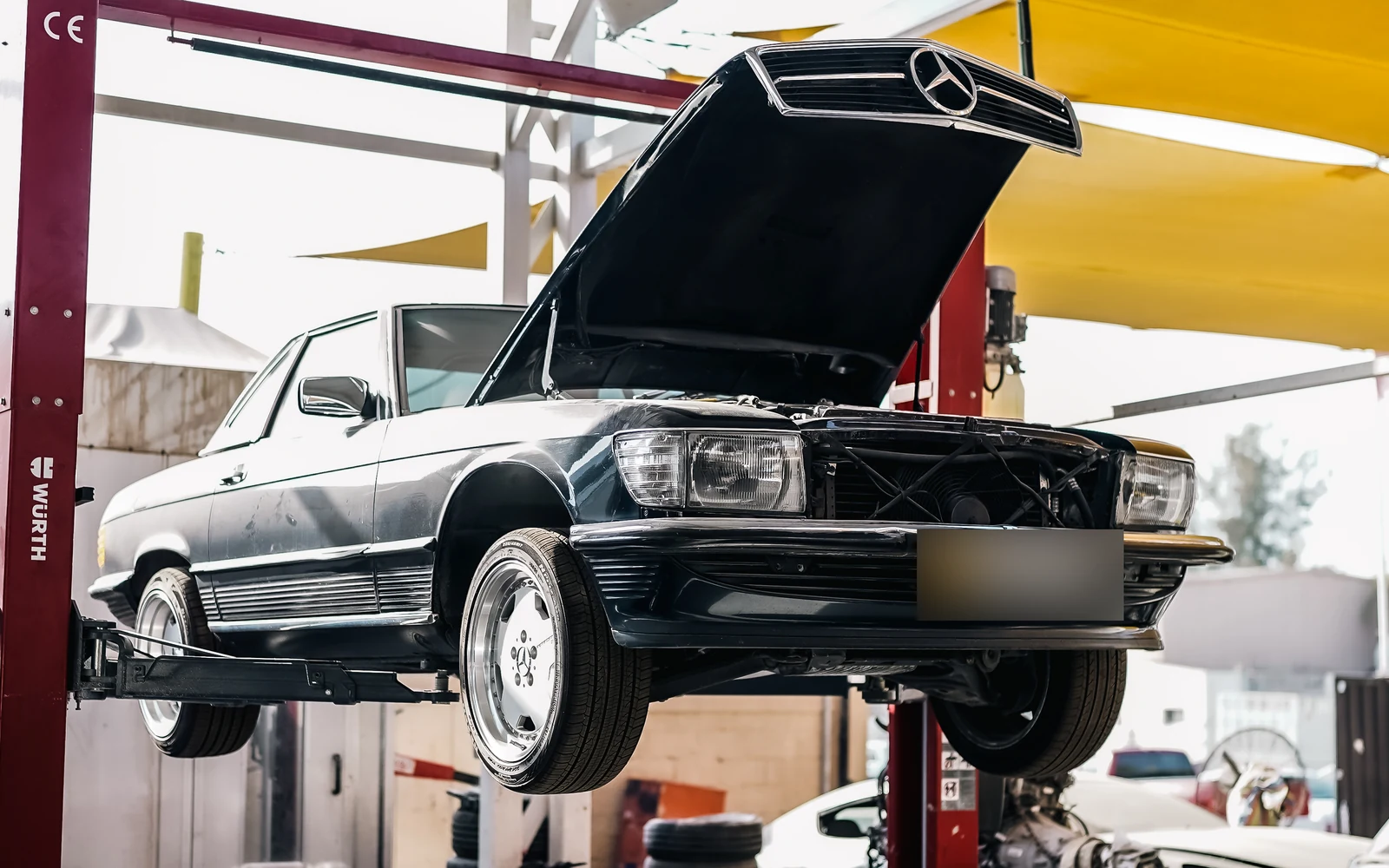 Classic Mercedes convertible on a workshop lift with its bonnet open.