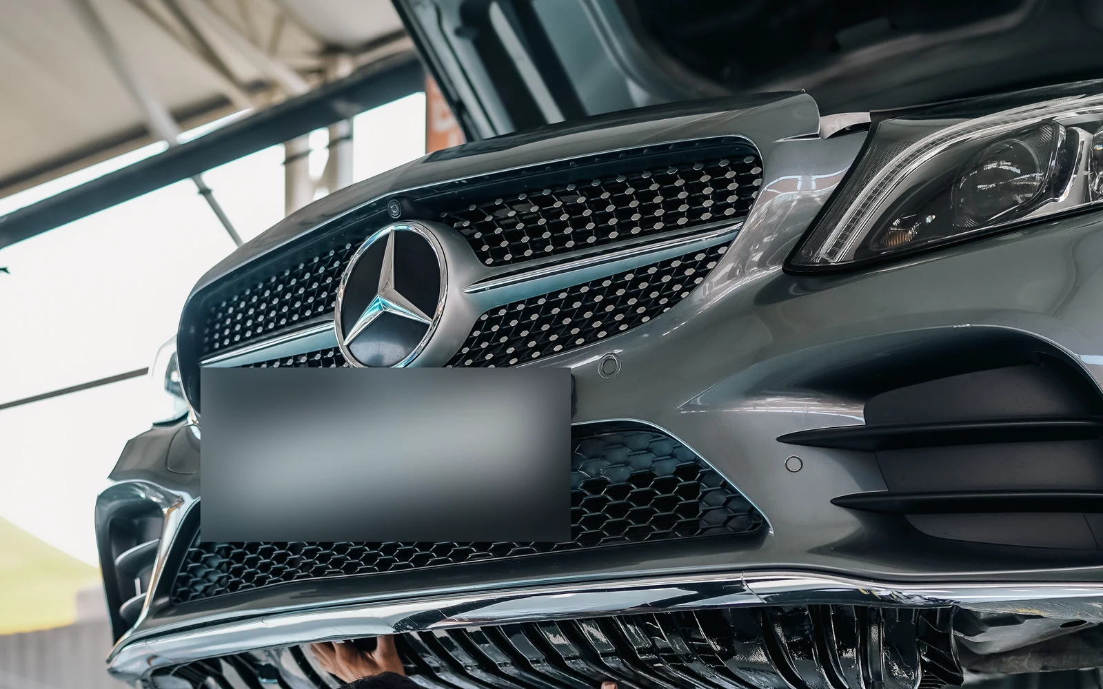Front view of a silver Mercedes raised on a workshop lift with its bonnet open.