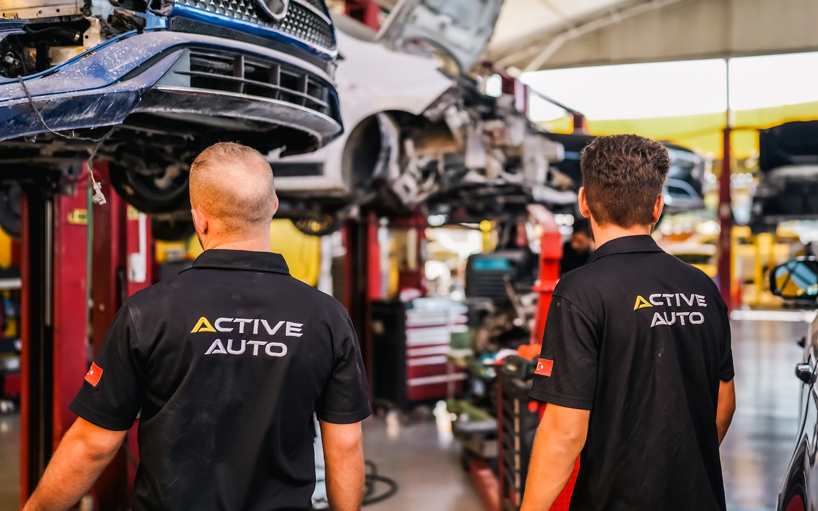 Two technicians working beneath cars raised on workshop lifts.