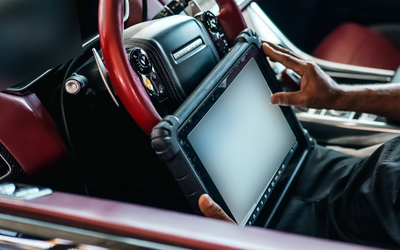 A diagnostic tablet held inside a Range Rover, with screen information obscured.