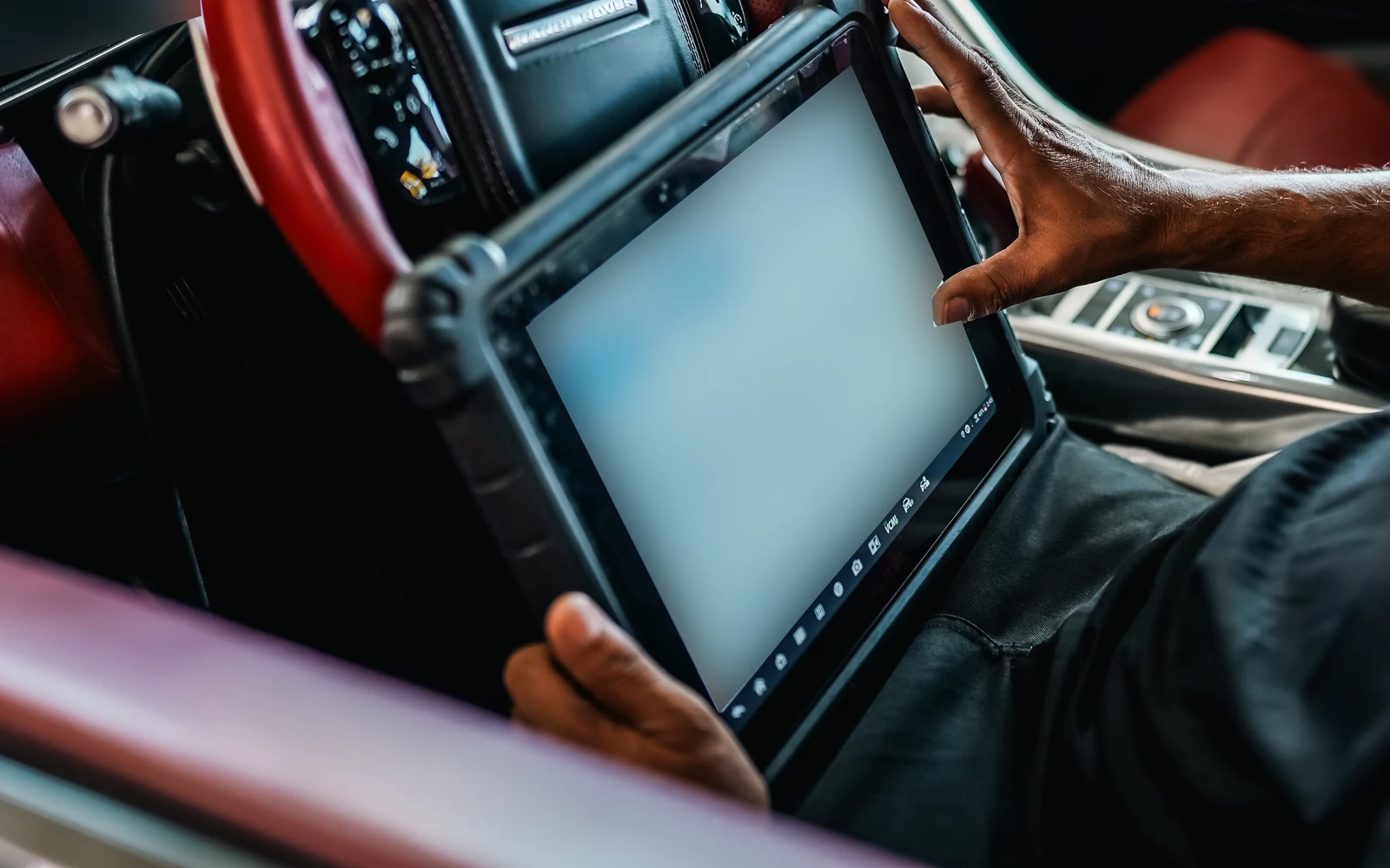 Close view of a diagnostic tablet beside a Range Rover steering wheel, with the display obscured.