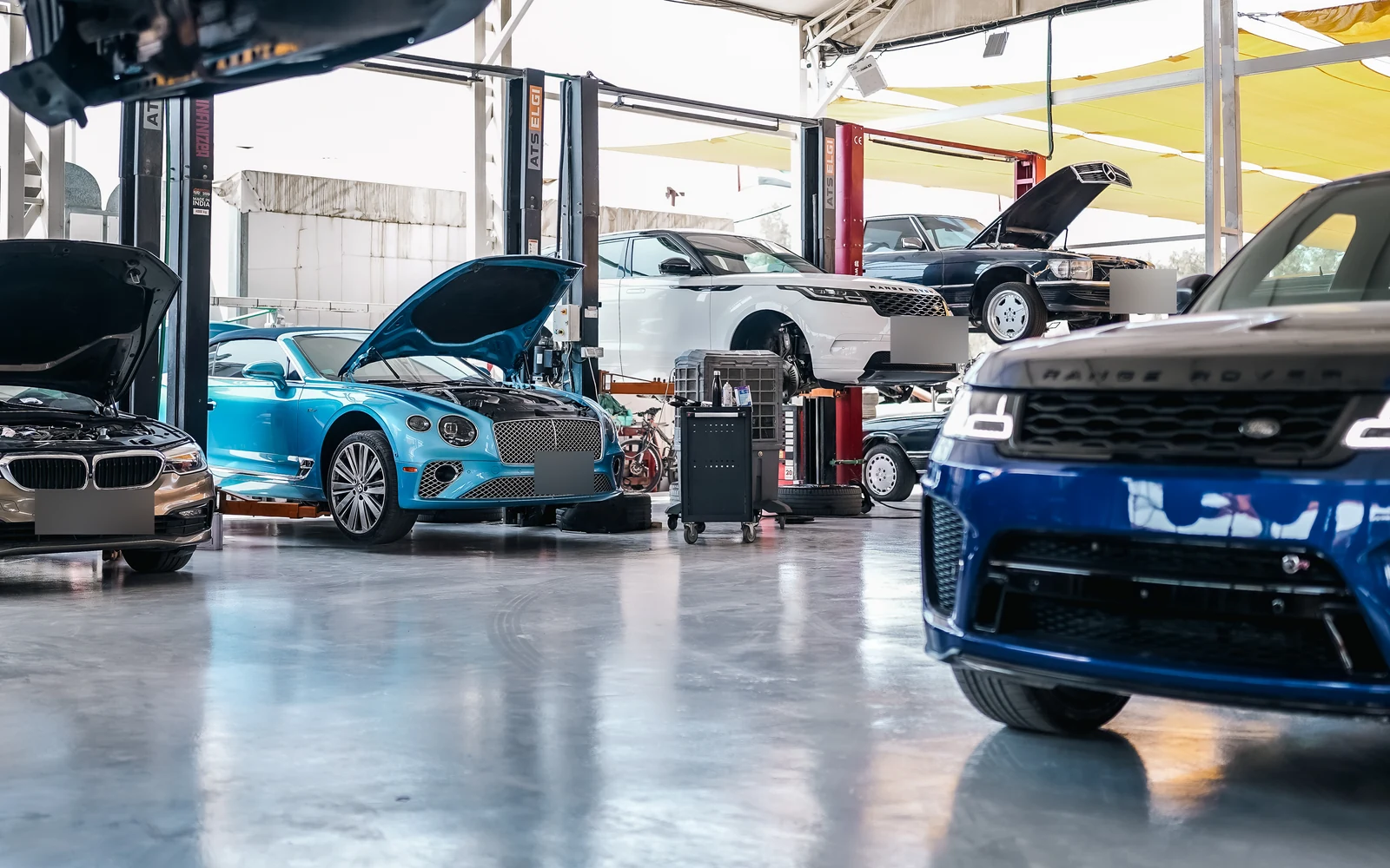 Cars and diagnostic equipment between the workshop lifts, with several bonnets open.