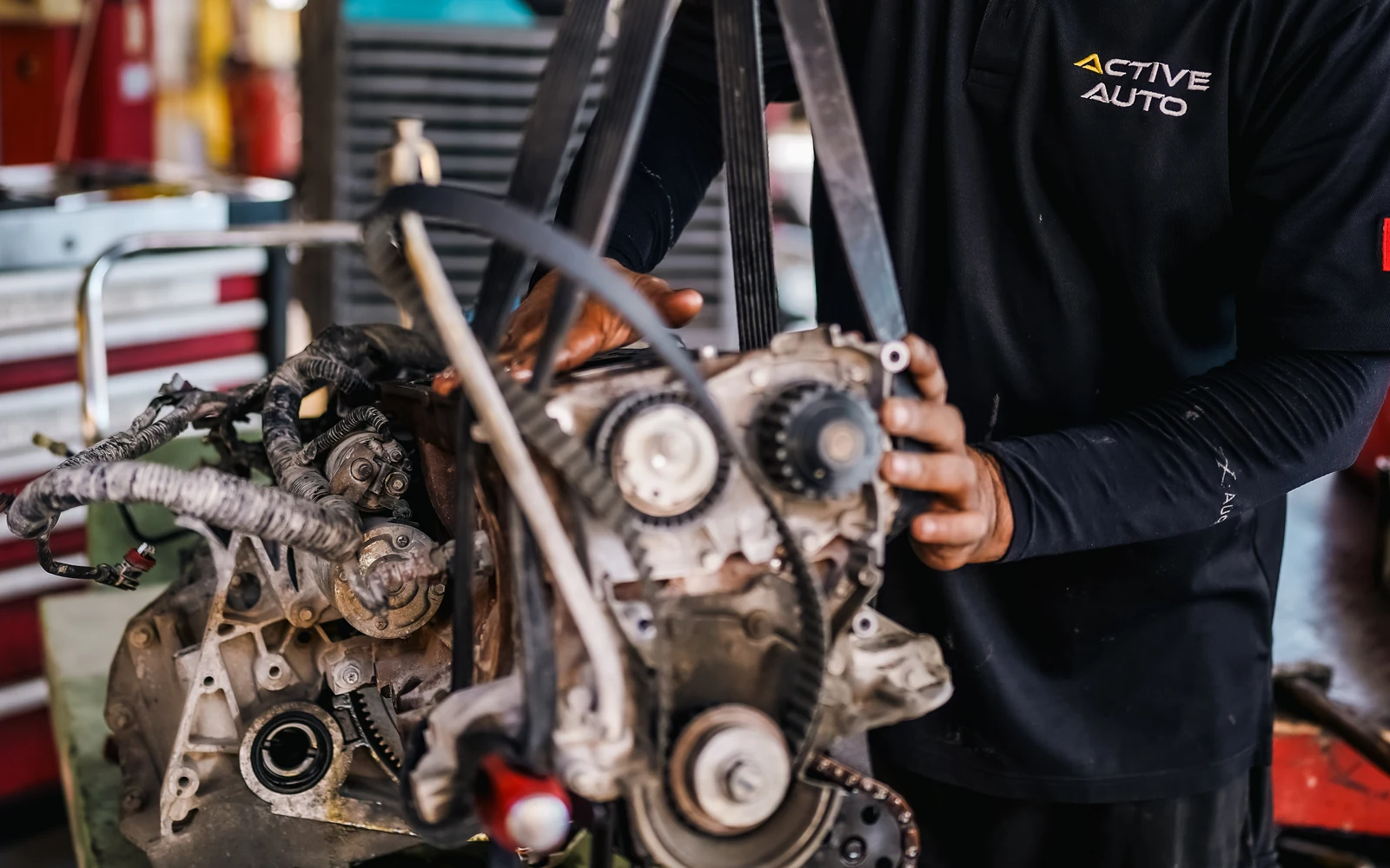A technician working on an engine assembly suspended outside a car.