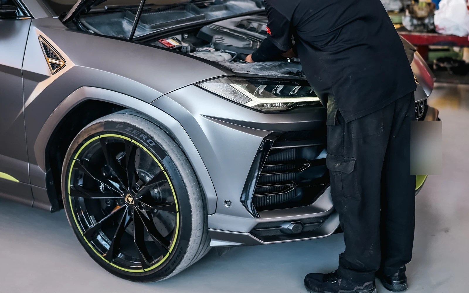 A technician leaning into the open engine bay of a Lamborghini SUV.