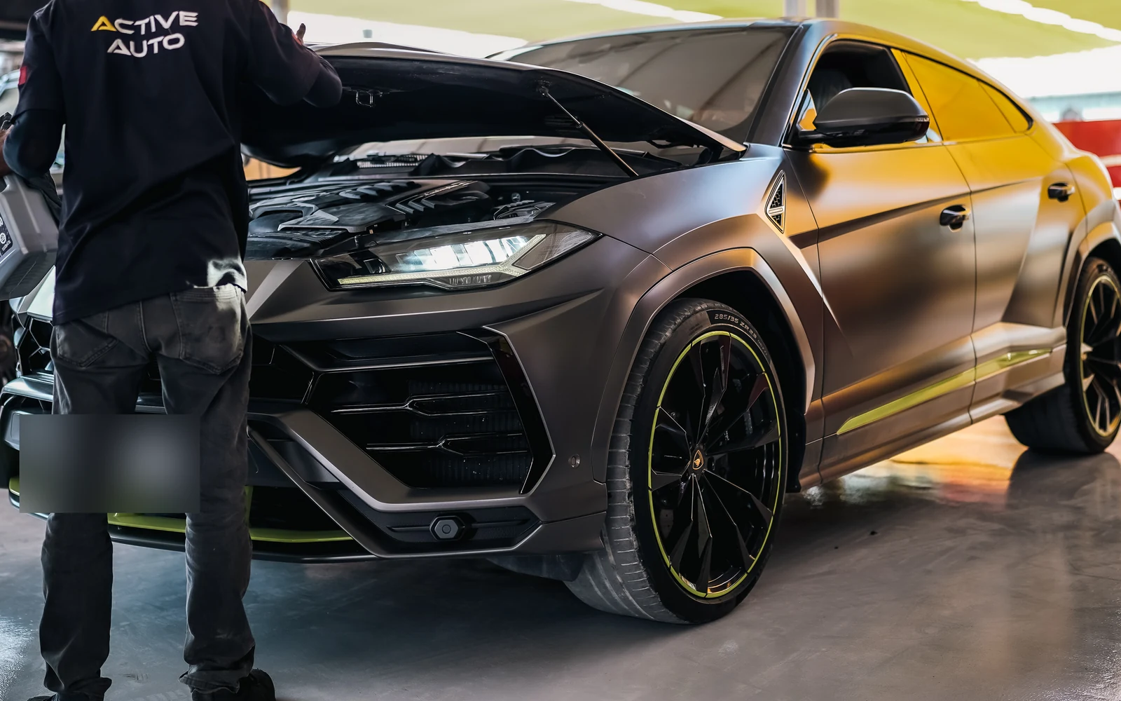 A Lamborghini SUV with its bonnet open beside a technician in the workshop.
