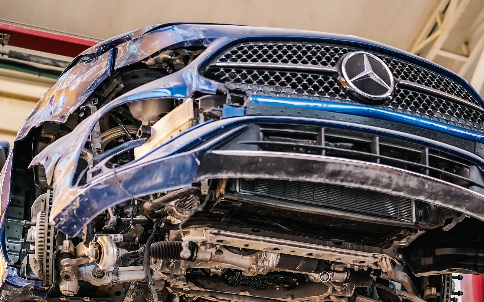 Front damage on a blue Mercedes raised on a lift, with lower components exposed.