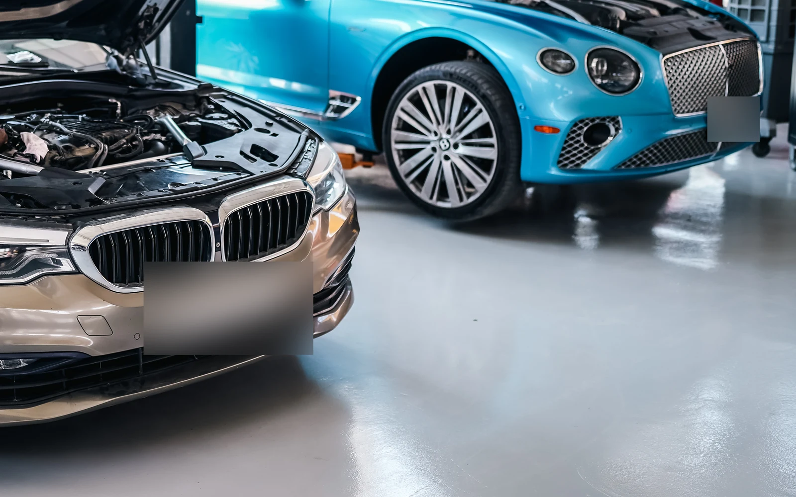 A BMW with its bonnet open beside a turquoise Bentley in the workshop.