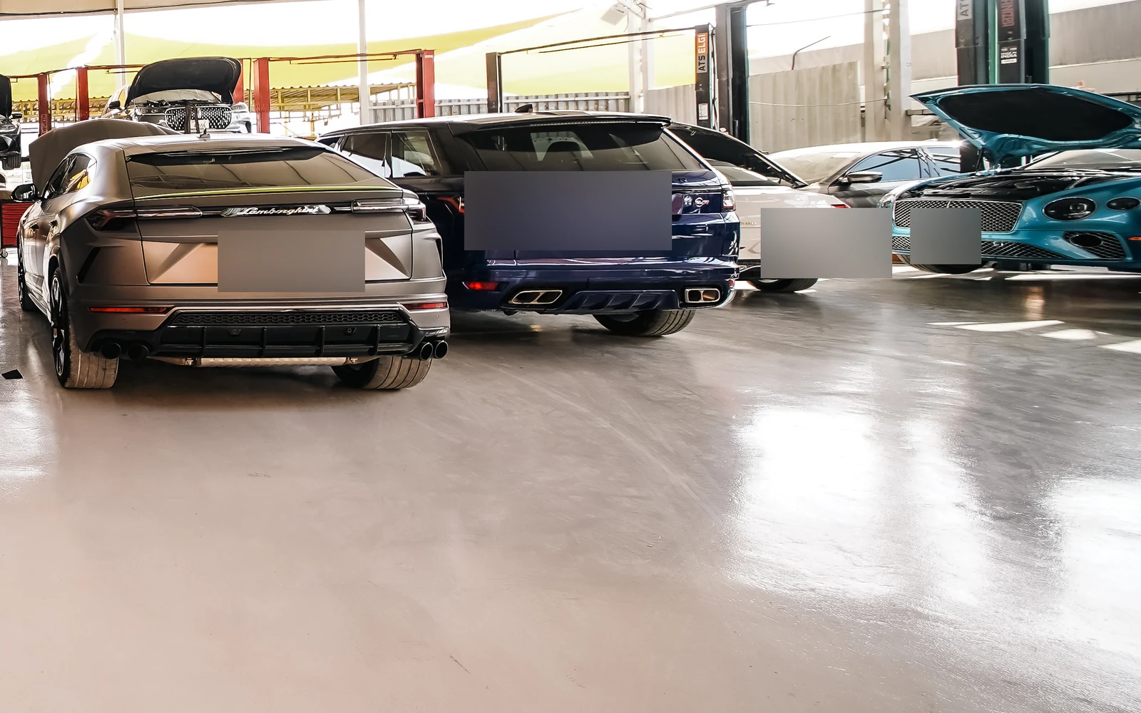 A row of cars inside the workshop, including Lamborghini and Range Rover rear views.